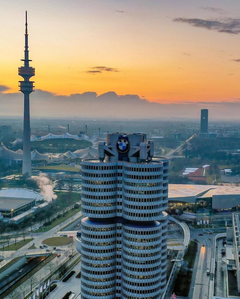 Dronenaufnahme eines Sonnenuntergangs in München mit Blick auf den Hauptsitz von BMW, dem Fernsehturm und dem Olympiapark im Hintergrund